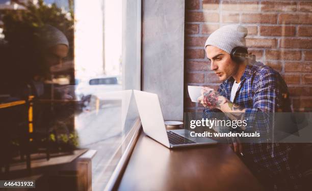 junger mann musik genießen, kaffee trinken, arbeiten auf seinem laptop - coffee shop chat stock-fotos und bilder