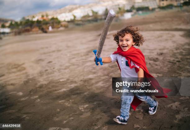 little boy with sword and cape running on the beach - toy sword stock pictures, royalty-free photos & images