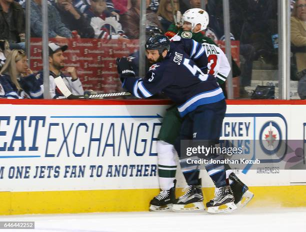 Mark Stuart of the Winnipeg Jets checks Eric Staal of the Minnesota Wild into the boards during first period action at the MTS Centre on February 28,...