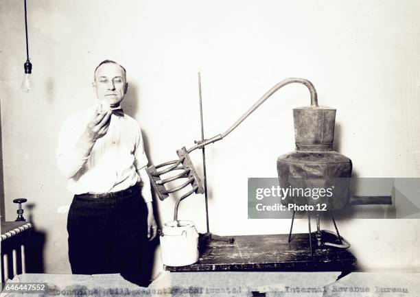 Moonshine still recently confiscated by the Internal Revenue Bureau photographed at the Treasury Department between 1921 and 1932. Man standing next...