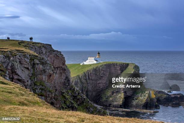 Walkers and the Stoer Head Lighthouse at the Point of Stoer in Sutherland, Scottish Highlands, Scotland, UK.