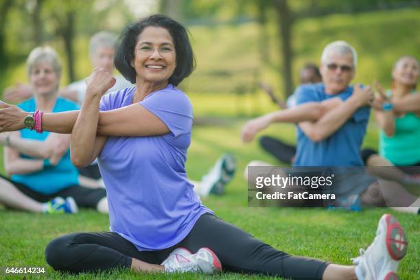 a group of senior adults are taking a fitness calss outside at the park. they are sitting on the grass and are stretching together. - couple doing yoga stock pictures, royalty-free photos & images