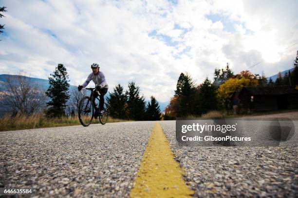 a male road cyclist rides along a country road in british columbia, canada in the fall. - crossing the road stock pictures, royalty-free photos & images