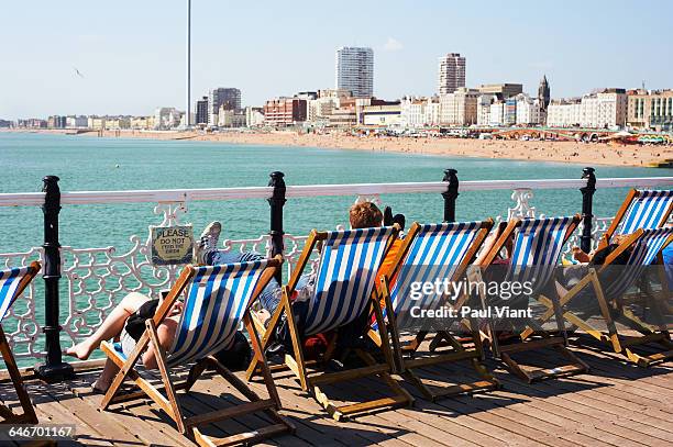 rear view holiday makers in deckchairs at brighton - brighton beach stock pictures, royalty-free photos & images