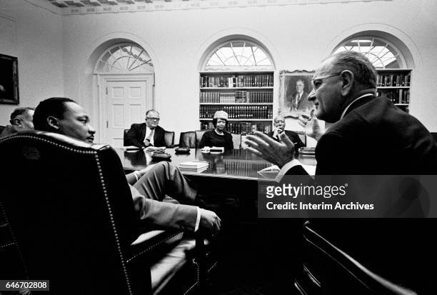 American Civil Rights leader Reverend Martin Luther King Jr listens to US President Lyndon Baines Johnson as they sit with others in the White...