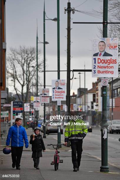 Man and two children walk past an election campaign posters in East Belfast on March 1, 2017. Voters in Northern Ireland will go to the polls on...