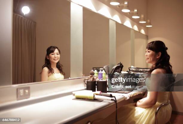 woman putting on make-up in front of mirror in dressing room - vestuario entre bastidores fotografías e imágenes de stock