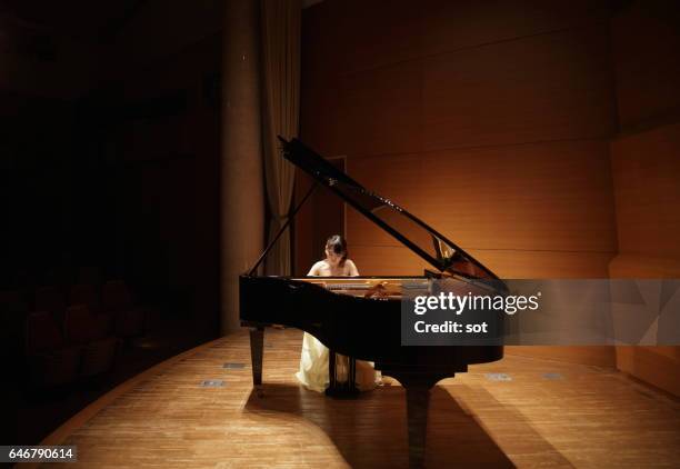 female pianist playing grand piano at concert hall stage - grand piano film stock-fotos und bilder