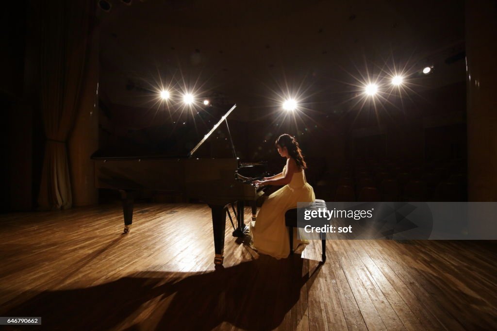 Female pianist playing grand piano at concert hall stage