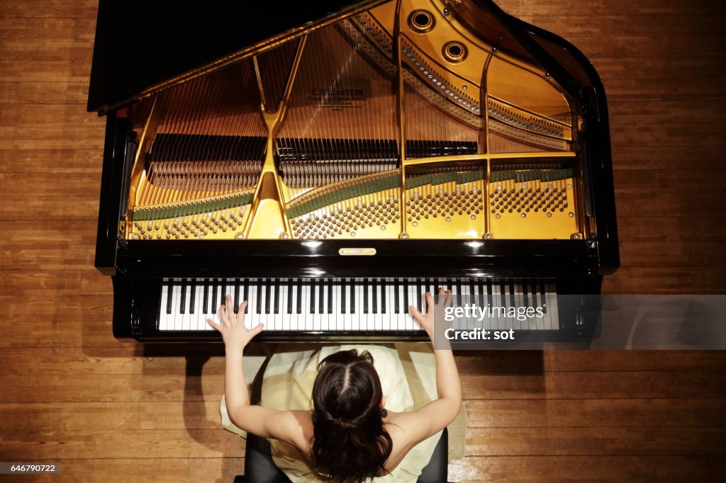 Female pianist playing grand piano at concert hall stage,aerial view