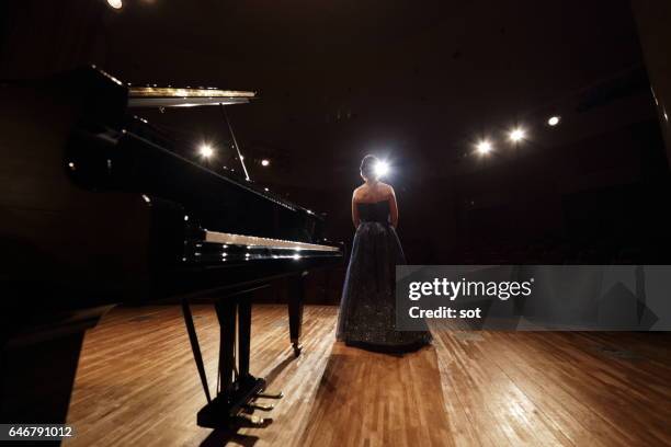 female pianist standing on concert hall stage with grand piano,rear view - concerto classico foto e immagini stock