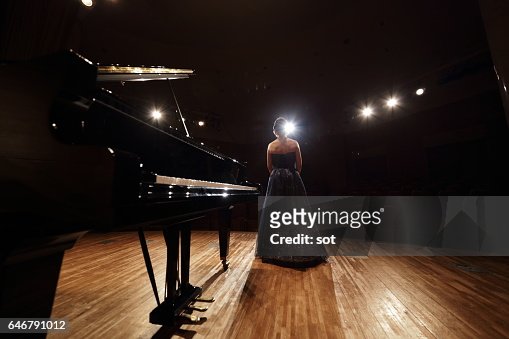 Female pianist standing on concert hall stage with grand piano,rear view