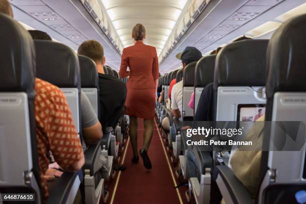female cabin crew walks away down aircraft cabin isle - steward stockfoto's en -beelden