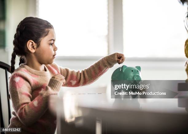girl (7 yrs) putting money in piggybank - kids money fotografías e imágenes de stock