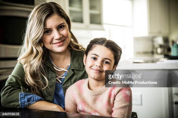 portrait of mother and daughter (7yrs) smiling, indoors - sitting at table looking at camera stock-fotos und bilder