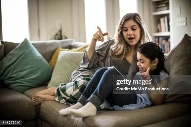 mother and daughter (7yrs) using tablet on couch - mother daughter couch imagens e fotografias de stock