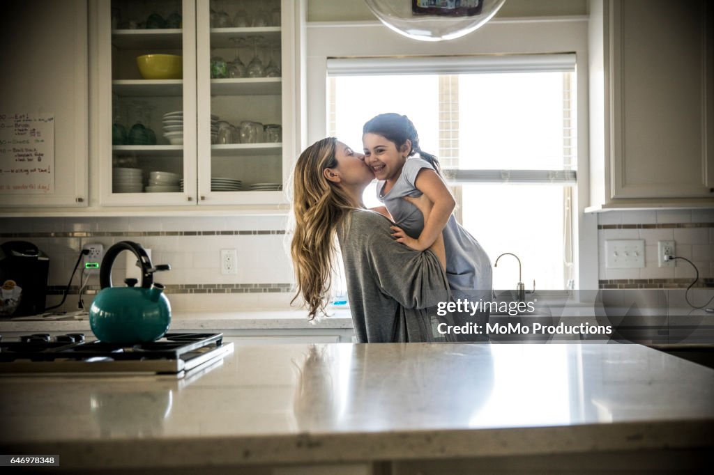 Mother kissing daughter (7yrs) in kitchen