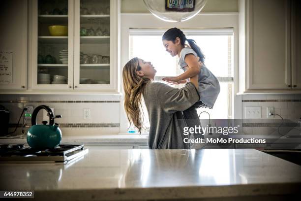 mother lifting daughter (7yrs) in kitchen - mother daughter kitchen stockfoto's en -beelden