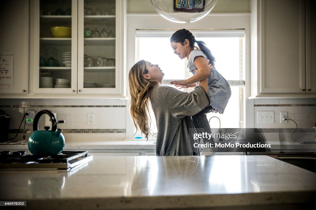 Mother lifting daughter (7yrs) in kitchen