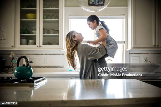 mother lifting daughter (7yrs) in kitchen - girl black hair room stock pictures, royalty-free photos & images