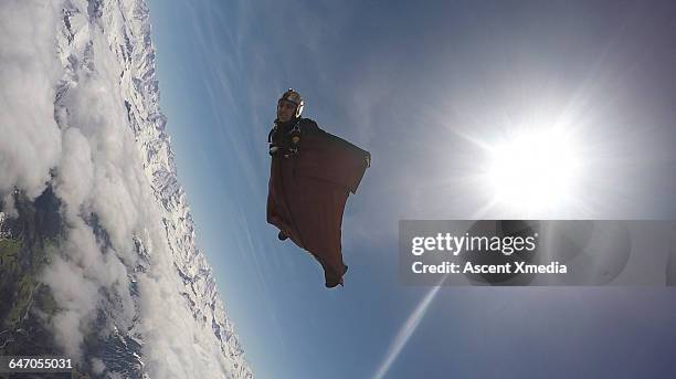 wingsuit flyer in mid-air flight over mountains - wing suit stock pictures, royalty-free photos & images