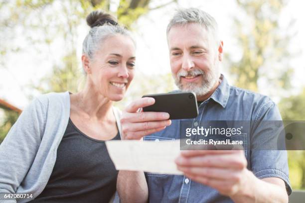 mature couple remote banking with phone - remote location stock pictures, royalty-free photos & images