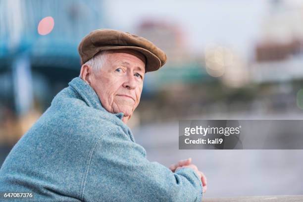 serious old man leaning on railing at waterfront - flat cap stock pictures, royalty-free photos & images