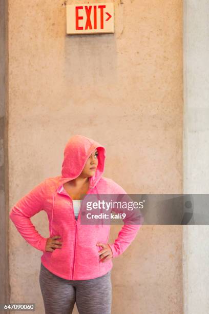 young mixed race hispanic woman standing under exit sign - hood clothing stock pictures, royalty-free photos & images