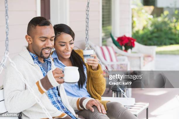 young mixed race couple drinking coffee on porch swing - swing chair stock pictures, royalty-free photos & images