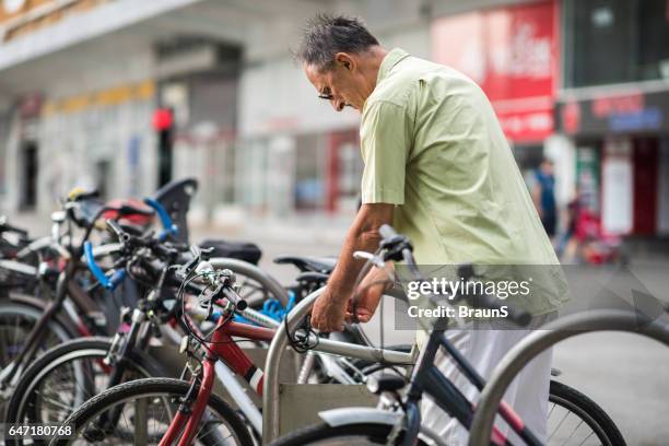 senior man locking his bicycle on a parking lot. - bicycle parking station stock pictures, royalty-free photos & images