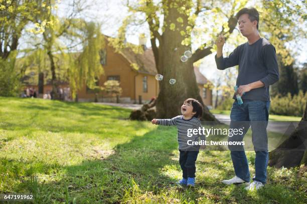 asian toddler boy chasing bubbles in green open space. - oslo play stock pictures, royalty-free photos & images