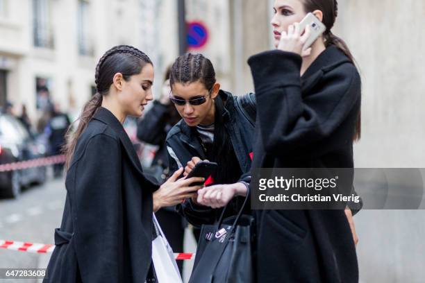 Models with braids searching for the way on their phone outside Balmain on March 2, 2017 in Paris, France.