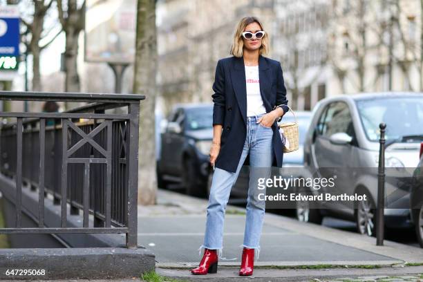 Anne-Laure Mais, fashion blogger from Adenorah, wears a black jacket, a white top, blue denim jeans pants, and red shoes, outside the Alexis Mabille...