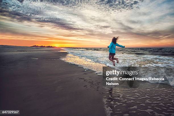 rear view of girl on beach at sunrise jumping in mid air - mobile alabama photos et images de collection