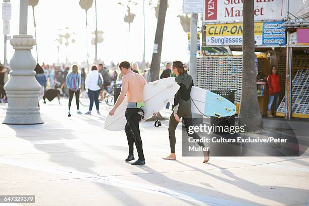 two male surfers wearing wetsuits carrying surfboards at venice beach, california, usa - cultura americana stock pictures, royalty-free photos & images