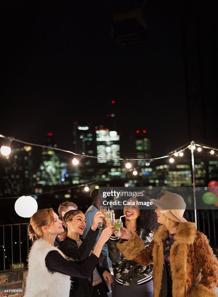 Young women toasting cocktails at nighttime rooftop party