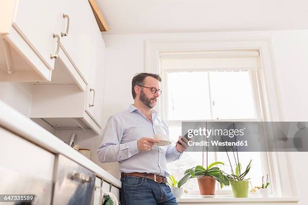 man standing in the kitchen with cup of coffee looking at his smartphone - low angle view home stock pictures, royalty-free photos & images