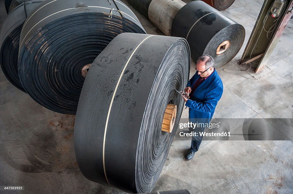 Manager with digital tablet in factory hall with rolls of rubber