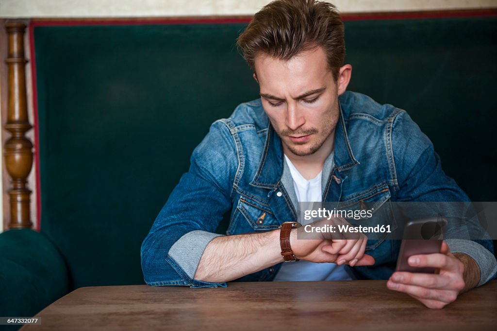 Portrait of angry young man sitting in a coffee shop checking the time