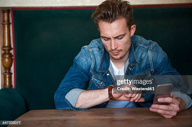 portrait of angry young man sitting in a coffee shop checking the time - man waiting foto e immagini stock