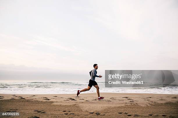 young man running on the beach - carrera fotografías e imágenes de stock