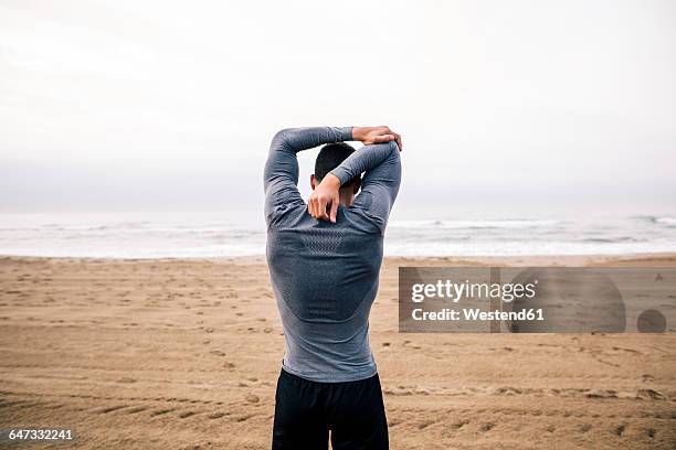 sportive young man stretching on the beach - back stretch stockfoto's en -beelden