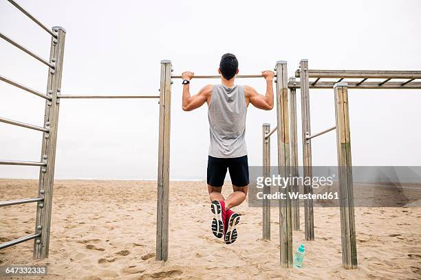 Young man doing chin-ups on the beach