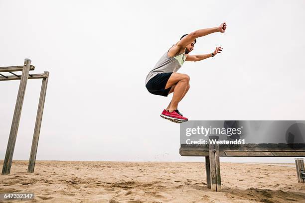 young man jumping on the beach - verspringen stockfoto's en -beelden