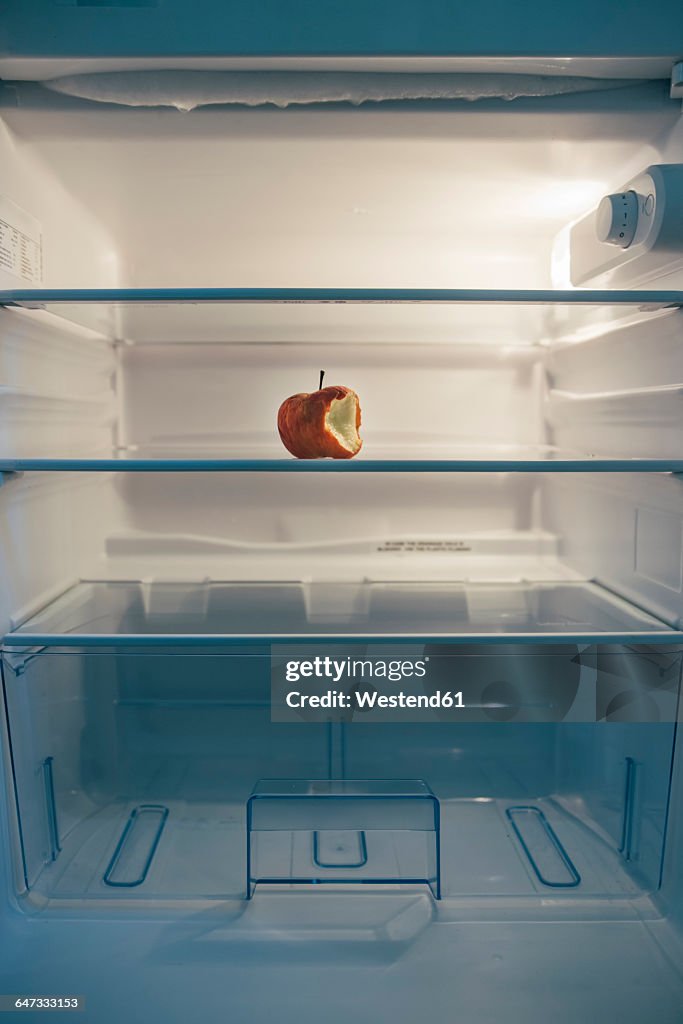 Nearly empty fridge with a seared bitten apple