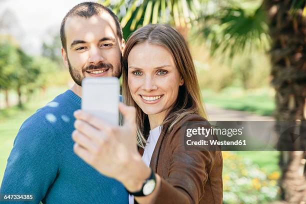 happy couple taking selfie with smartphone in a botanical garden - botanischer garten stock-fotos und bilder