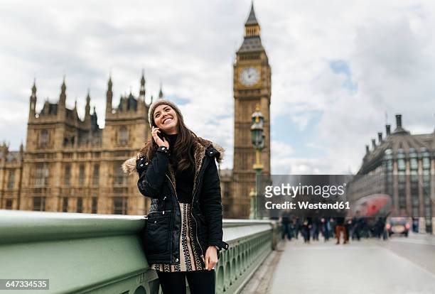 uk, london, happy young woman telephoning with smartphone in front of palace of westminster - person falls from westminster bridge stock-fotos und bilder