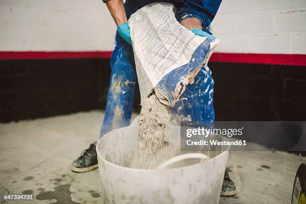 bricklayer pouring cement powder in bucket - zement stock-fotos und bilder