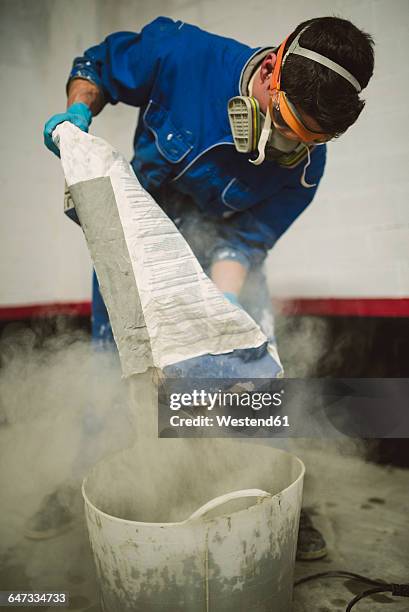 bricklayer pouring cement powder in bucket - sacchi cemento foto e immagini stock