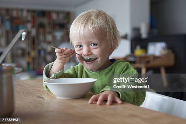 portrait of smiling little boy eating soup at home - soup on spoon imagens e fotografias de stock